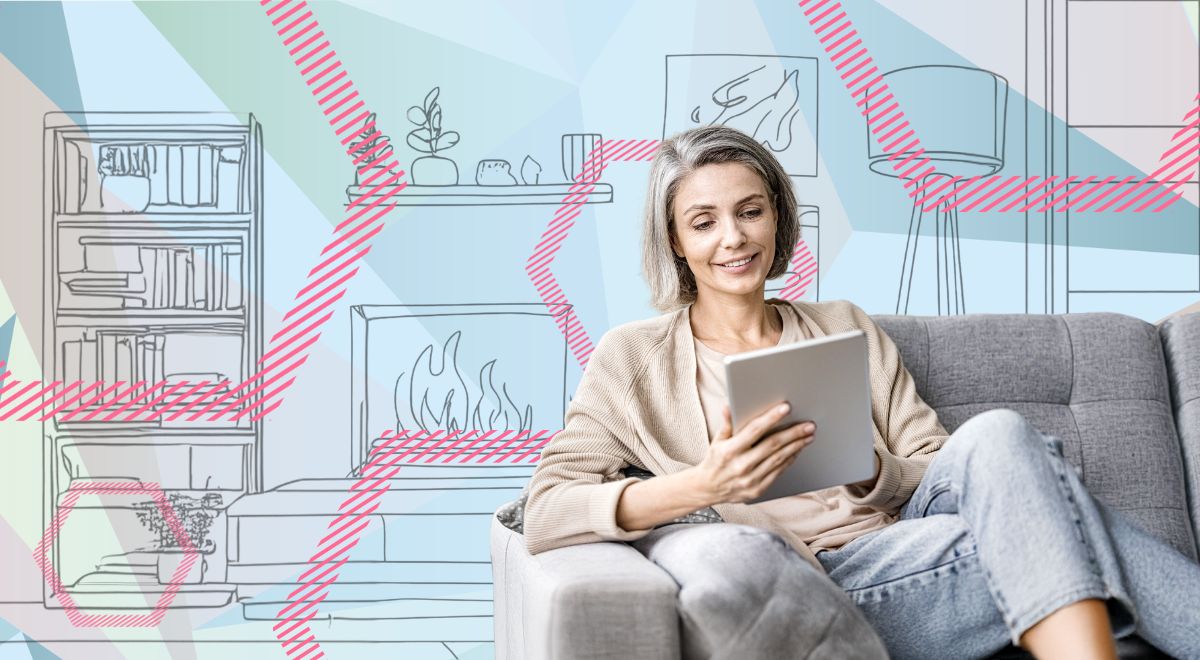 Frau sitzt mit einem Tablet auf einem grauen Sofa.