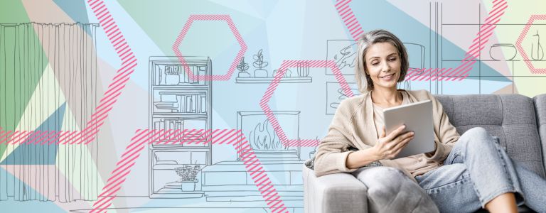 Frau sitzt mit einem Tablet auf einem grauen Sofa.